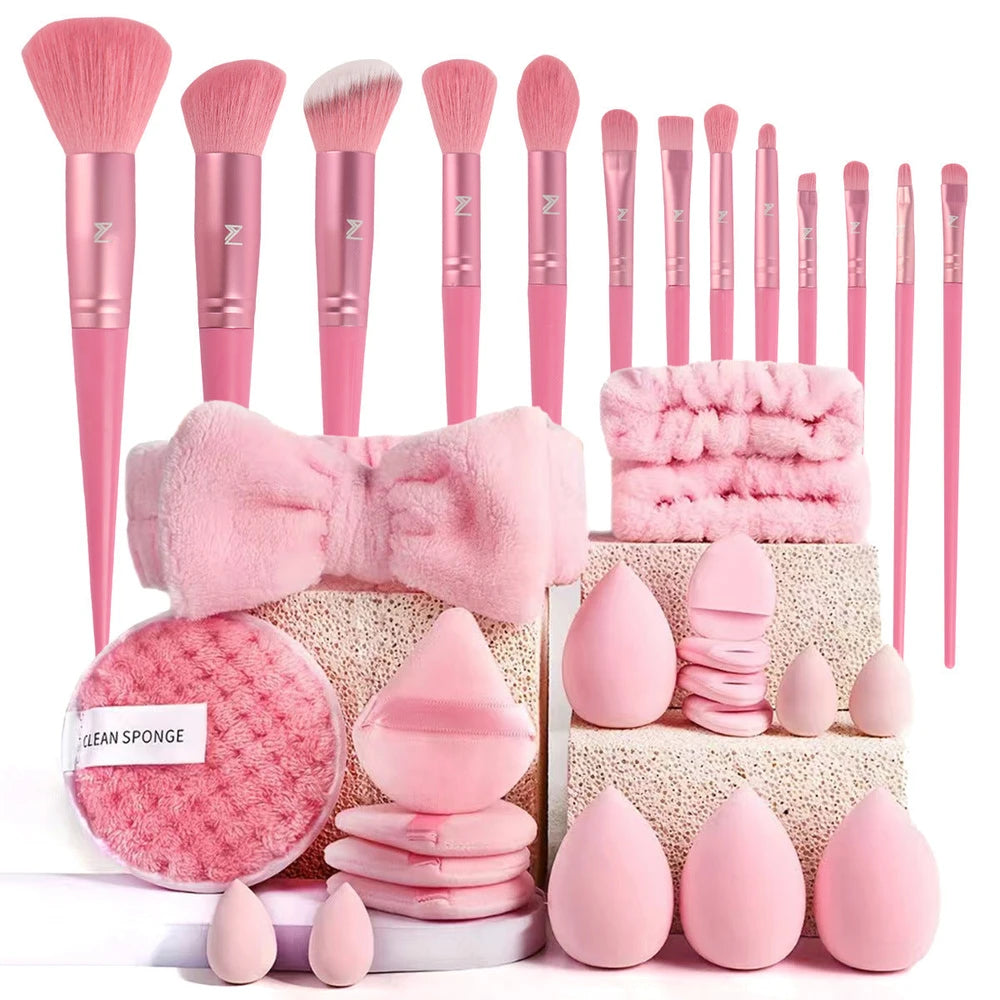 Set of pink makeup brushes and accessories including a bow, sponges, and a scrubber.