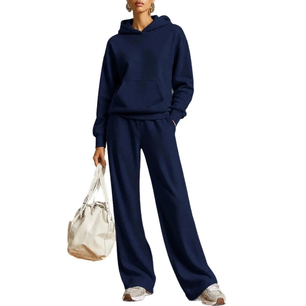 A woman modeling a matching navy blue hoodie and wide-leg sweatpants set, holding a cream tote bag against a plain white background.