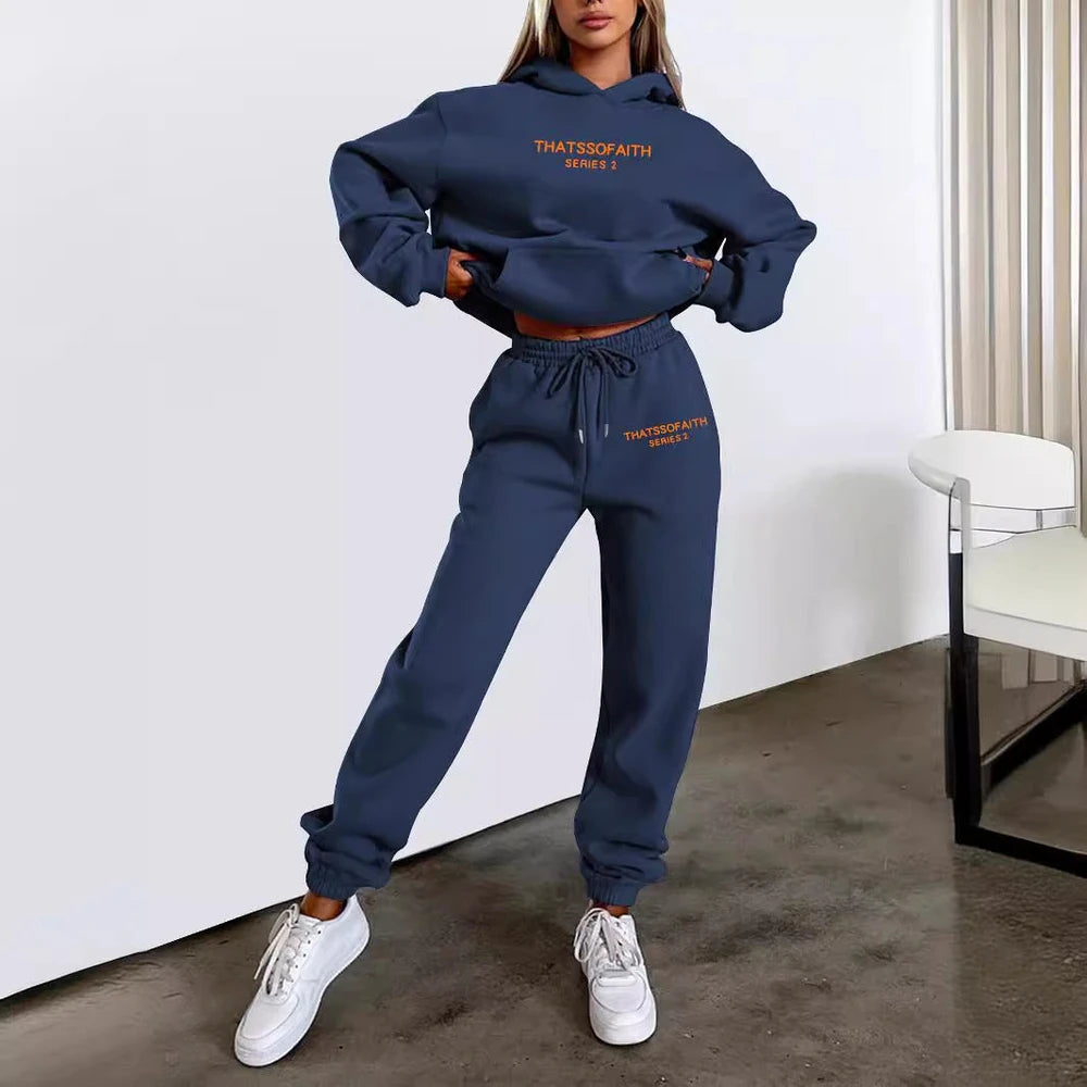 Person wearing a navy blue tracksuit with 'THATSSOFAITH' branding in a minimalistic room.