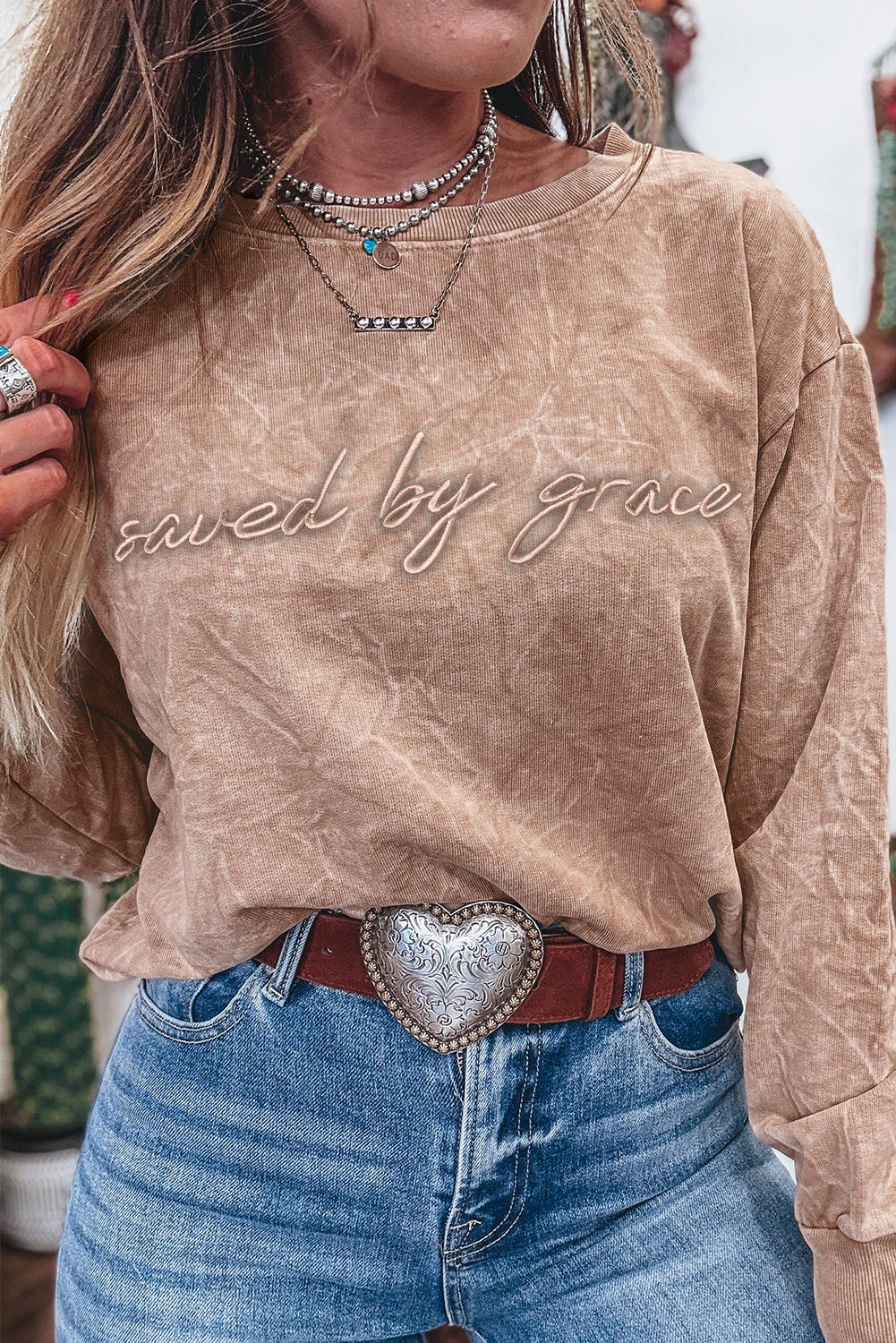 Beige long-sleeve sweatshirt with “Saved by Grace” script lettering, styled with blue jeans