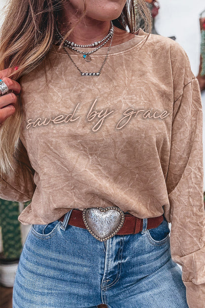 Beige long-sleeve sweatshirt with “Saved by Grace” script lettering, styled with blue jeans