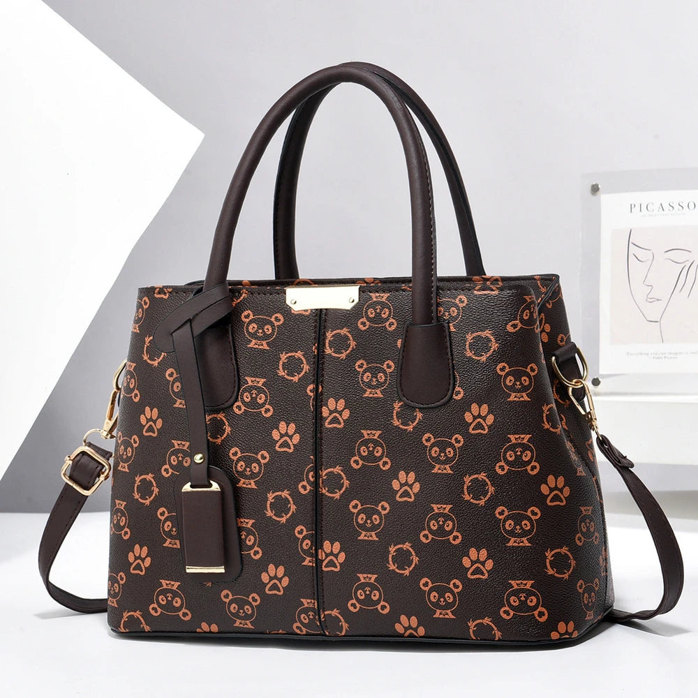 Dark brown faux leather tote bag with a tan bear and paw print pattern, two top handles, gold-tone hardware, and a shoulder strap.