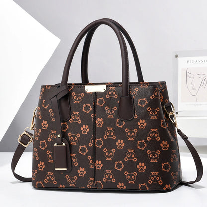 Dark brown faux leather tote bag with a tan bear and paw print pattern, two top handles, gold-tone hardware, and a shoulder strap.