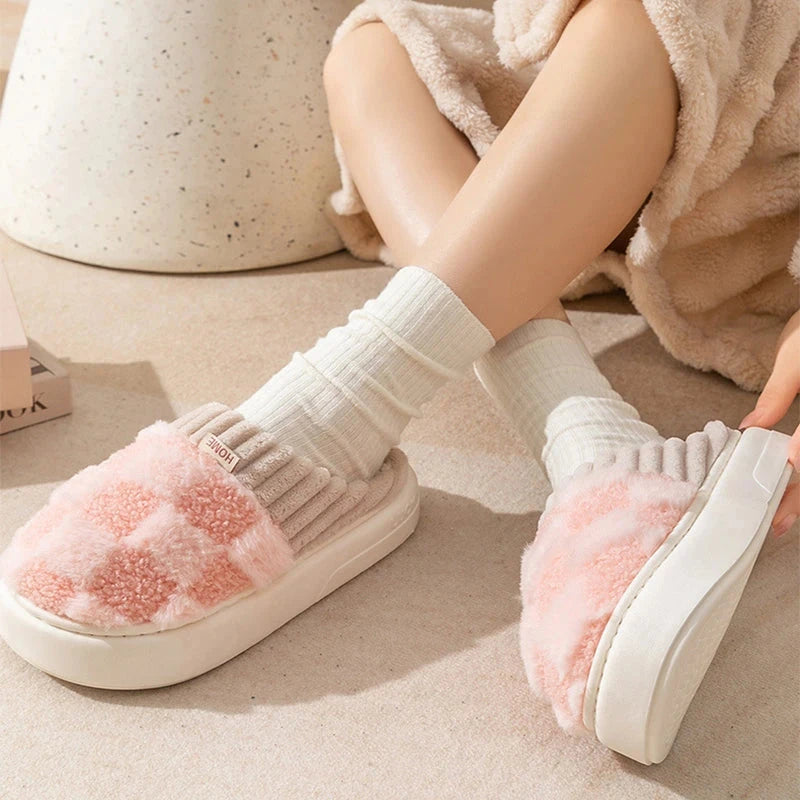 White slippers with pink fuzzy sole worn by a person on a light wooden floor.