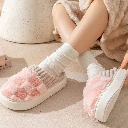 White slippers with pink fuzzy sole worn by a person on a light wooden floor.