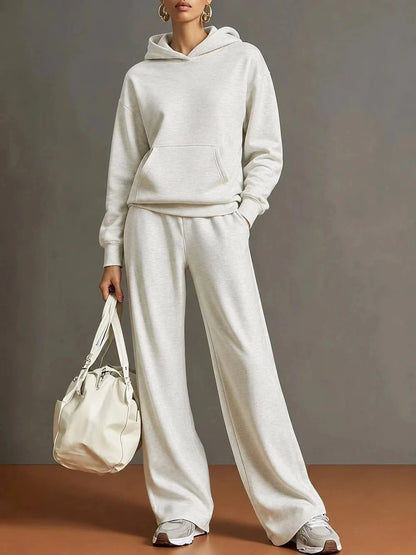 A model wearing a matching light beige/cream two-piece loungewear set consisting of a pullover hoodie and wide-leg sweatpants