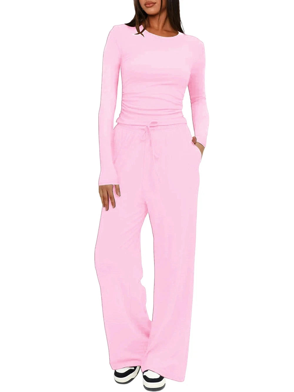 A woman modeling a light pink two-piece loungewear set consisting of a long-sleeve crewneck top and matching wide-leg drawstring pants, shown against a plain white background.