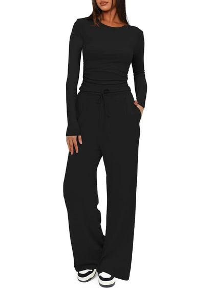 A woman modeling a black long-sleeve top and matching wide-leg drawstring pants against a plain white background.