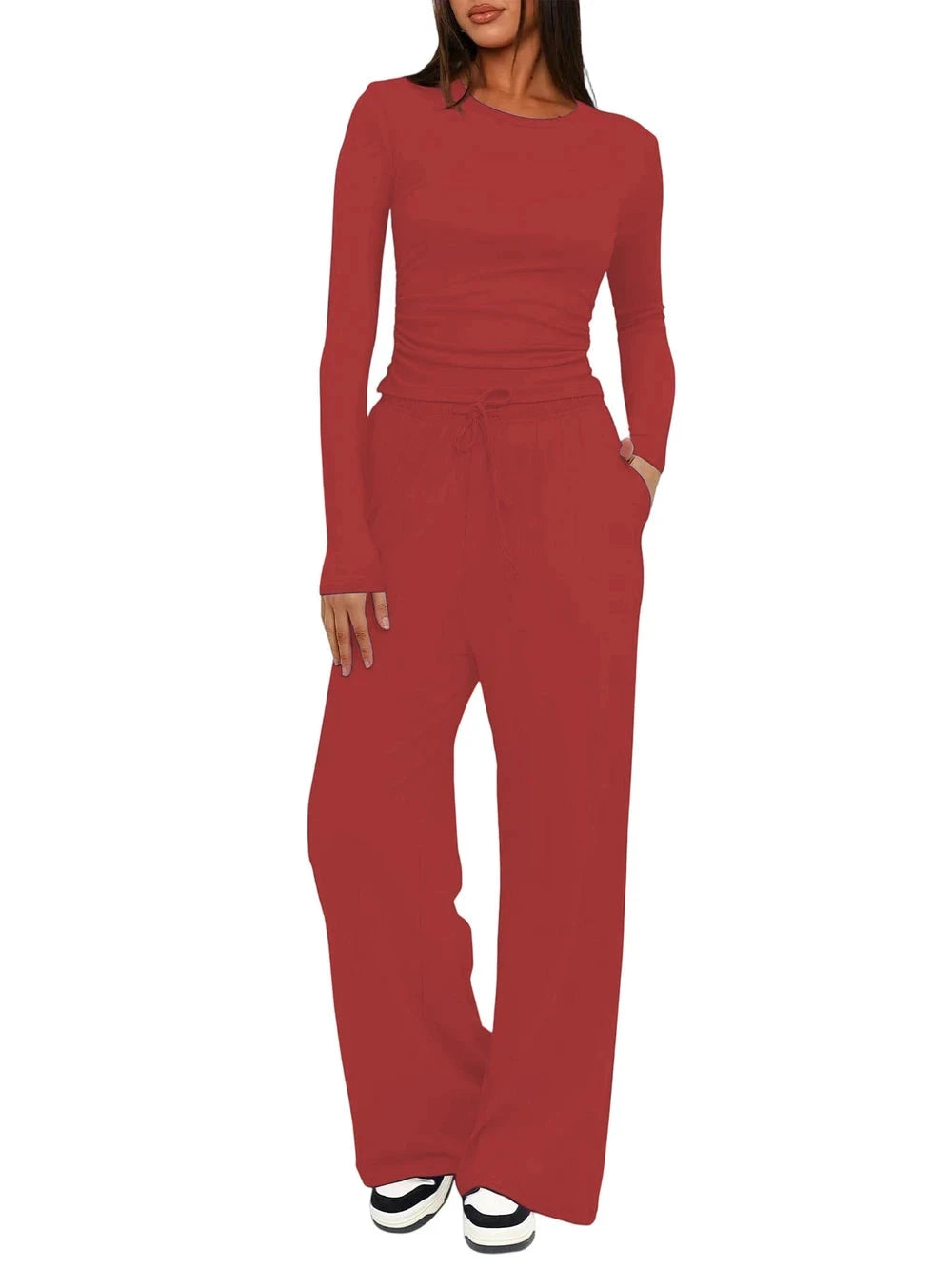 A woman modeling a matching two-piece outfit consisting of a long-sleeve crewneck top and high-waisted wide-leg pants in a solid rust red color, shown against a plain white background.