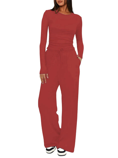 A woman modeling a matching two-piece outfit consisting of a long-sleeve crewneck top and high-waisted wide-leg pants in a solid rust red color, shown against a plain white background.