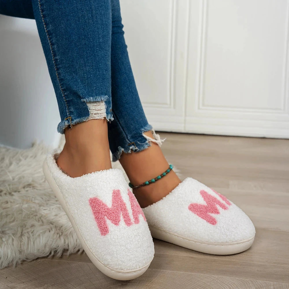 White slippers with pink text worn indoors on a wooden floor.