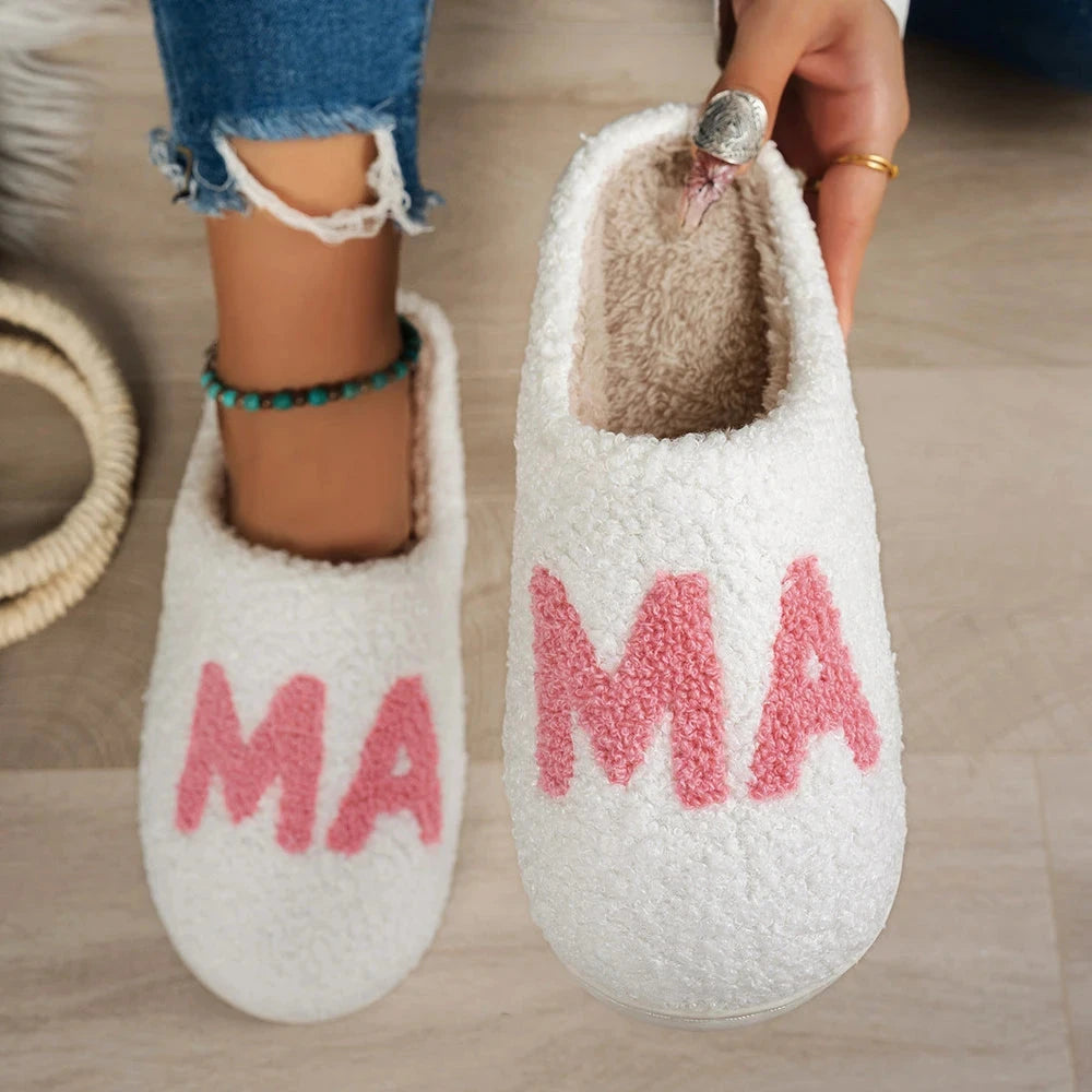 White fuzzy slippers with pink “MA” lettering and plush beige lining, shown worn with jeans and held up to show the inside.