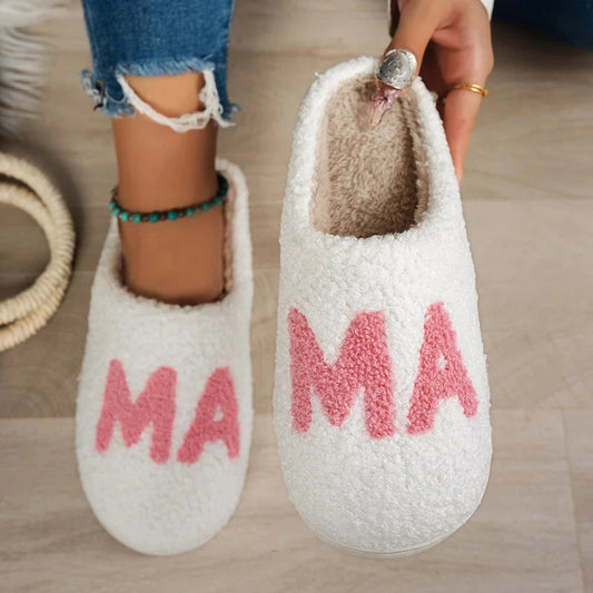 White fuzzy slippers with pink “MA” lettering and plush beige lining, shown worn with jeans and held up to show the inside.