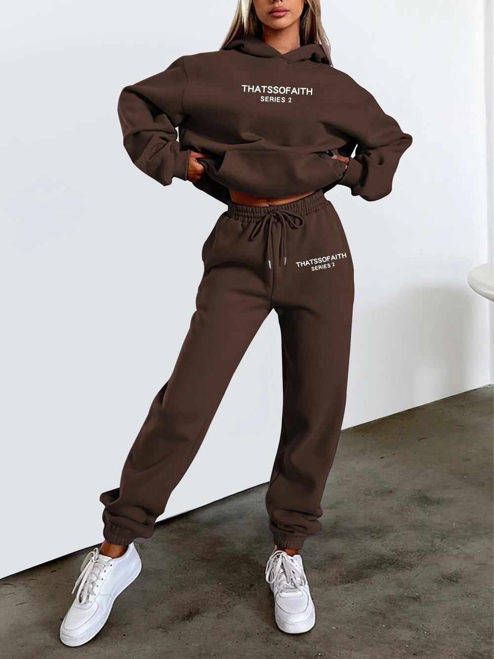 Person wearing a black 'THATSSSFAITH' hoodie and pants set with white sneakers on a plain background.
