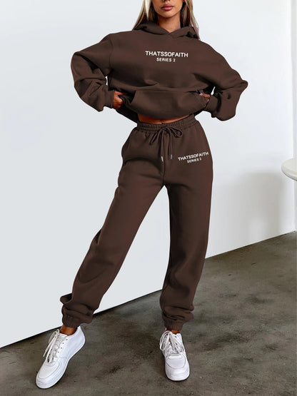 Person wearing a black 'THATSSSFAITH' hoodie and pants set with white sneakers on a plain background.