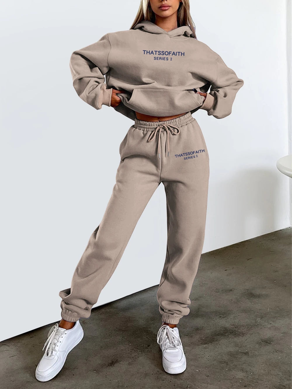 Person wearing a beige tracksuit with text on it, standing against a white background.
