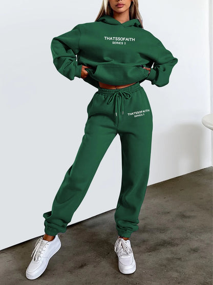 Person wearing a green  'THATSSSFAITH' hoodie and pants set with white sneakers on a plain background.