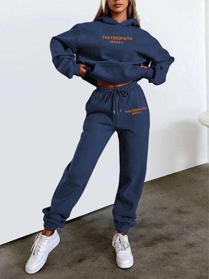 Person wearing a navy blue tracksuit with text on it, standing against a white wall.
