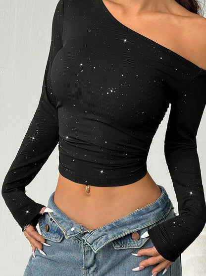  Black fitted long-sleeve crop top with an asymmetric off-shoulder neckline and sparkling accents, styled with blue jeans.