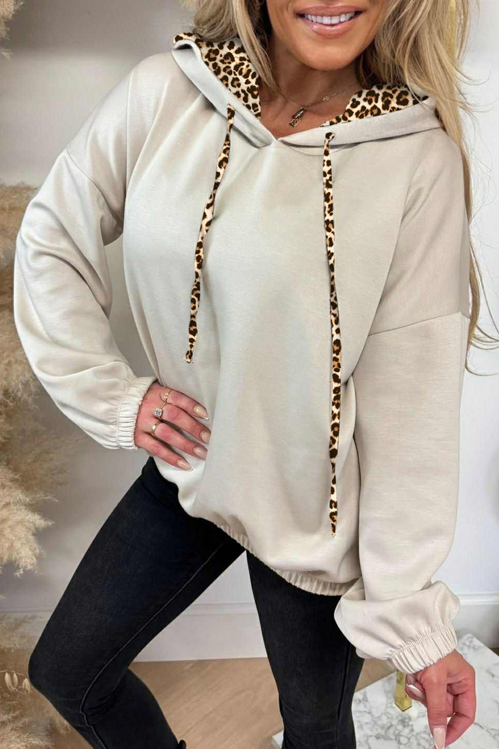 Cream pullover hoodie with leopard print hood lining and drawstrings, styled with black pants.